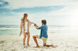 © JordaanExams/peopleimages.com - Marriage, proposal and couple with love at beach for engagement, happiness and surprise on vacation. Blue sky, waves and man with question on knee for romantic gesture, support and holiday in Venice