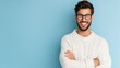 © Trusha - A man with glasses is smiling and wearing a white sweater. He is standing in front of a blue wall