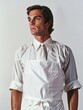 © vefimov - Man wearing white apron, standing confidently with hands on hips in kitchen. Professional cook working.