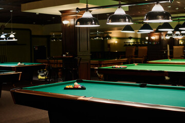 part of spacious hall in modern bar or pub with two rows of green billiards tables with balls inside