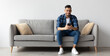 © Prostock-studio - Cool Gadget And Application. Portrait of young smiling Arab man holding mobile phone, typing sms message, sitting on the couch in living room. Guy browsing internet, surfing web, using app, free space