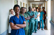 © Sachin - Diverse team of confident healthcare professionals standing in hospital corridor, led by smiling African American nurse in blue scrubs