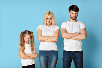 A family of three stands in front of a light blue background with their arms crossed. The young girl has a frustrated expression on her face. In the middle is the mother appears to be annoyed.