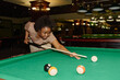 © pressmaster - Young active woman in casual attire bending over pool table and looking at one of balls before hitting it with cue while playing billiards
