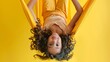 © PondLord - A young girl hanging playfully upside down in an aerial yoga hammock, her hair cascading towards the ground, showcasing the fun and accessible nature of the practice against a cheerful yellow