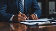 © AlfaSmart - Businessman in a suit signing a contract on a wooden desk, with a focus on his hands and the pen