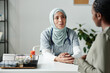 © pressmaster - Young female gynecologist in hijab looking at pregnant African American woman keeping hand on belly while supporting her
