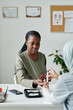 © pressmaster - Young African American pregnant woman keeping hand over workplace of clinician checking her glucose level with digital medical device