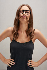 Wall Mural - Hair, moustache and silly woman with comedy, laughing and funny joke with glasses in studio. Happy, excited and playful with humor and prank with comic kiss and crazy person with grey background