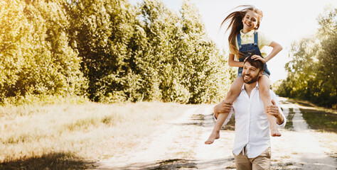 Wall Mural - Joyful Dad Carrying Little Daughter During After-Quarantine Family Walk In Countryside On Summer Weekend Day.