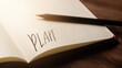© Jakub - A handwritten inscription 'Plan' on a grille of an open notebook on a wooden countertop, next to a black pencil, lighting of light. (selective focus), translation: plan
