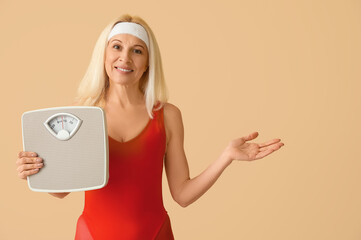 Poster - Sporty mature woman with scales showing something on beige background