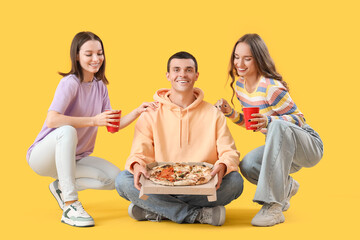 Poster - Young friends with tasty pizza and beer on yellow background