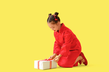 Canvas Print - Cute little Asian girl with gift sitting on yellow background. Chinese New Year celebration