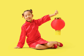 Wall Mural - Cute little Asian girl with lantern sitting on yellow background. Chinese New Year celebration