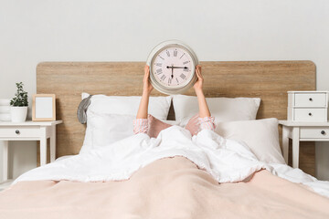 Poster - Young woman lying on bed and holding clock in bedroom