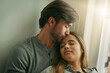 © Sanc/peopleimages.com - Couple, kiss and relax by window in house for comfort, love and bonding time together with trust and care. Man, woman and hug or cuddle in home for connection, relationship and support on weekend