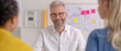 © TH_Stock - A smiling manager with engages in a positive discussion with colleagues in a bright office, with project plans and sticky notes visible in the background.