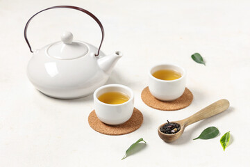 Poster - Teapot with cups, wooden spoon of dry tea and leaves on white background