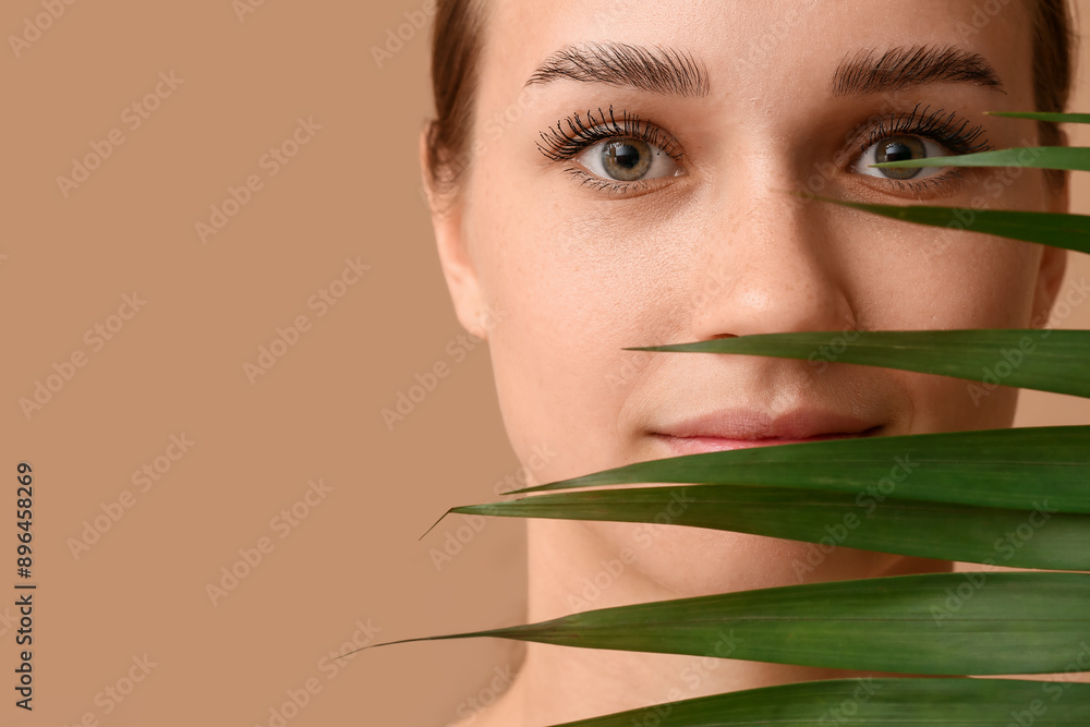 Young woman with beautiful eyebrows and palm leaf on brown background