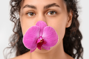 Wall Mural - Beautiful young African-American woman with purple orchid flower on white background, closeup