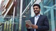 © The Little Hut - Focused successful mature Indian or Latin entrepreneur businessman holding digital pc tablet standing outdoor at business office building Hispanic smiling man in suit working using tou : Generative AI