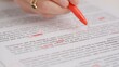 © kinomaster - Professional school or college teacher grades a homework exam papers of students. Woman checks essay, crosses many wrong words, corrects it with red pen.