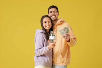 Poster - Young couple with jar and money for car hugging on yellow background