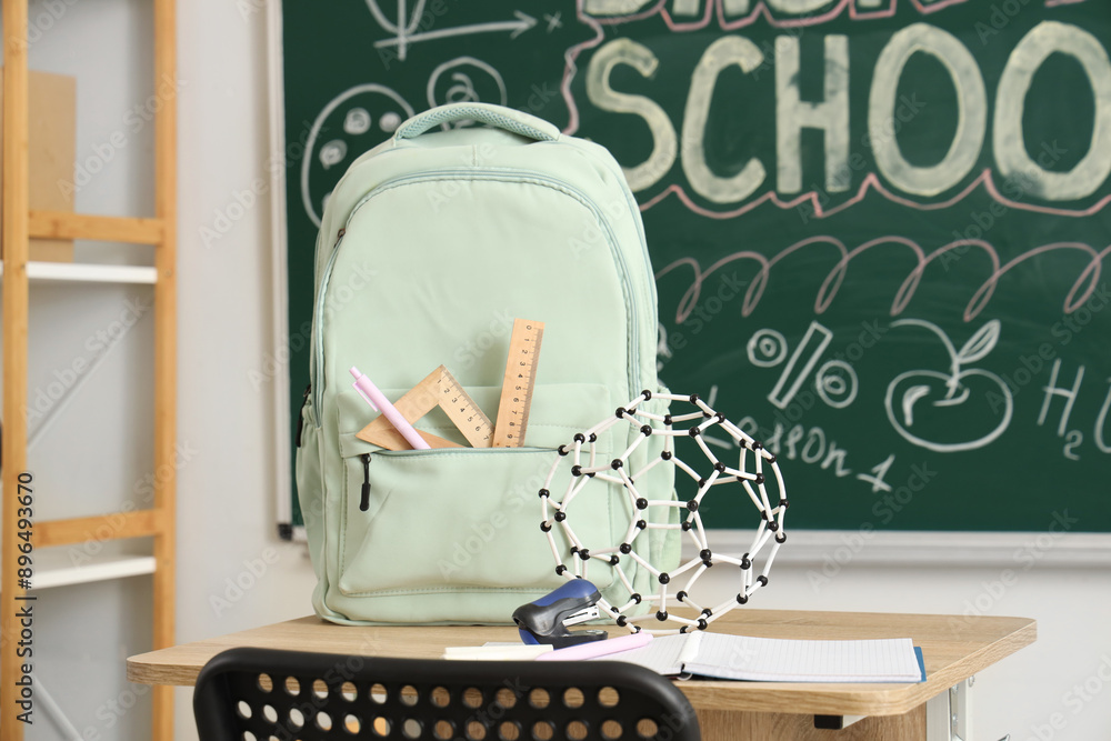School desk with backpack and notebook in light classroom