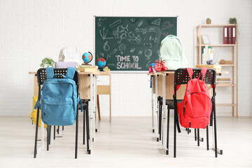 Wall Mural - School desks, backpacks and blackboard in light classroom