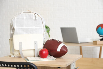 Wall Mural - School desk with apple, backpack, rugby ball and notebook in light classroom