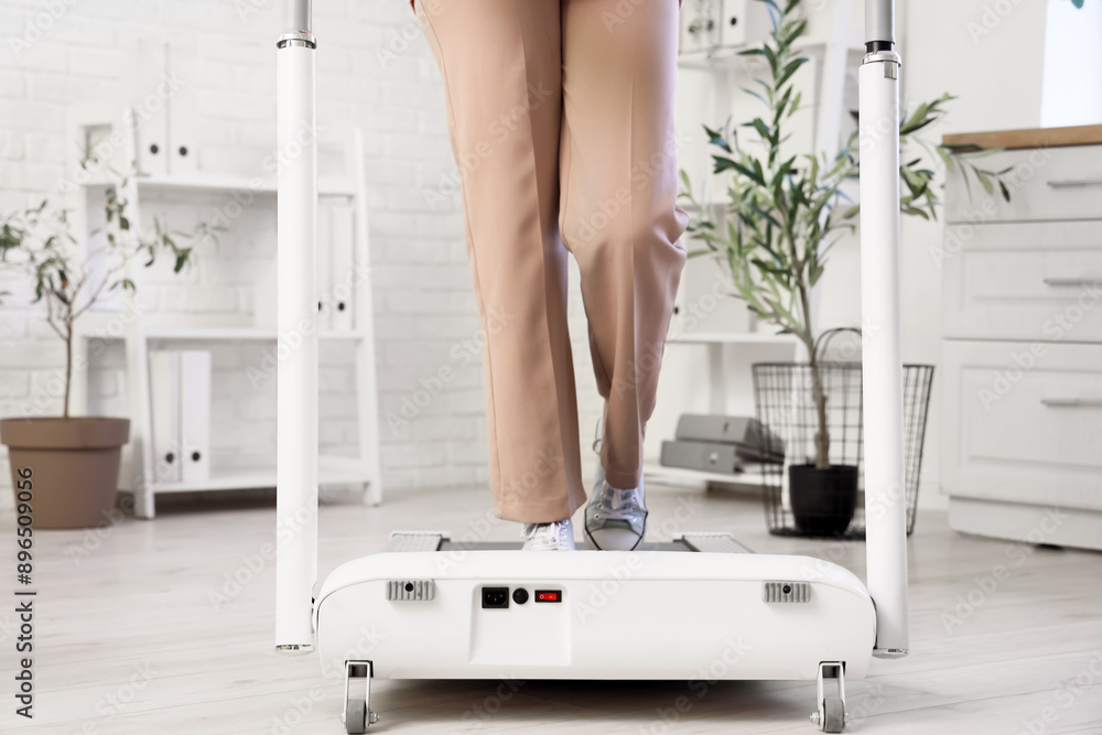 Young businesswoman training on treadmill in office