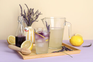 Wall Mural - Glass and jug of fresh lavender lemonade with flowers and wooden juicer on colorful background