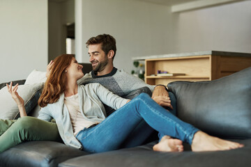 Poster - Couple, home and smile on sofa in living room for bonding, care and support as lovers. House, people and happy or laugh for relationship on couch in love on break, relax and rest in comfort