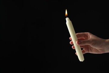 Wall Mural - Woman holding burning candle on black background, closeup. Space for text