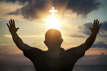 Wall Mural - silhouette of man praying with cross on sunset sky background.