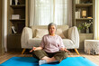 © CandyRetriever  - Happy Asian senior mature woman meditating in lotus pose in living room. Wellbeing elderly grandmother enjoy healthy lifestyle relaxing with meditation deep breath and practicing yoga exercise at home
