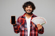 © ViDi Studio - Young happy Indian man he wear red shirt casual clothes use blank screen mobile cell phone hold fan of cash money in dollar banknotes isolated on plain grey color background studio. Lifestyle concept