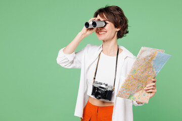 Traveler shocked amazed woman wear casual clothes read map use binocular look aside isolated on plain green background. Tourist travel abroad in free spare time rest getaway. Air flight trip concept.