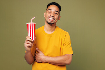 Wall Mural - Young man of African American ethnicity wears yellow t-shirt casual clothes hold in hand cup of soda pop cola fizzy water isolated on plain pastel green background studio portrait. Lifestyle concept.