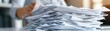 © Pnitha - Close up of a stack of white paper documents on a desk, a business woman working with a pile in the office