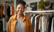 © Nadin Faust - smiling middle aged woman standing in front of a fashion store, posing with her outfit while stylish outfits hang in the background, showcasing a beautiful black woman