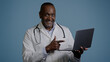 © Yuliia - African american man doctor therapist ethnic male surgeon in white coat in blue background studio working on laptop consulting patient online remote diagnostics take useful information from internet