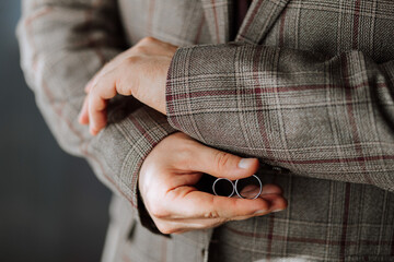 A man is wearing a plaid jacket and holding two wedding rings in his hand. Concept of formality and celebration, as the man is likely getting ready for a wedding or another special occasion