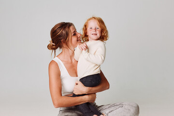 Wall Mural - Mother and daughter bonding moment sitting on floor in front of white background with copy space