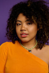 Beautiful African American woman in orange top and necklace poses against vibrant backdrop.