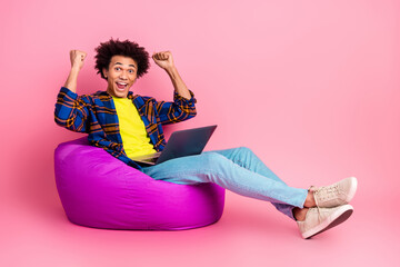 Wall Mural - Photo of cheerful positive young man wear clothes use netbook sit soft pouf success isolated on pink color background