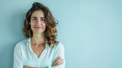 Wall Mural - A woman with her arms crossed, smiling at the camera on light blue background