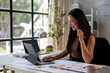 © Wasana - A woman is sitting at a desk with a laptop and a pen