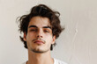 © Владимир Солдатов - A young man with long curly brown hair and light stubble, looking at the camera with a neutral expression, wearing a white t-shirt, light textured background